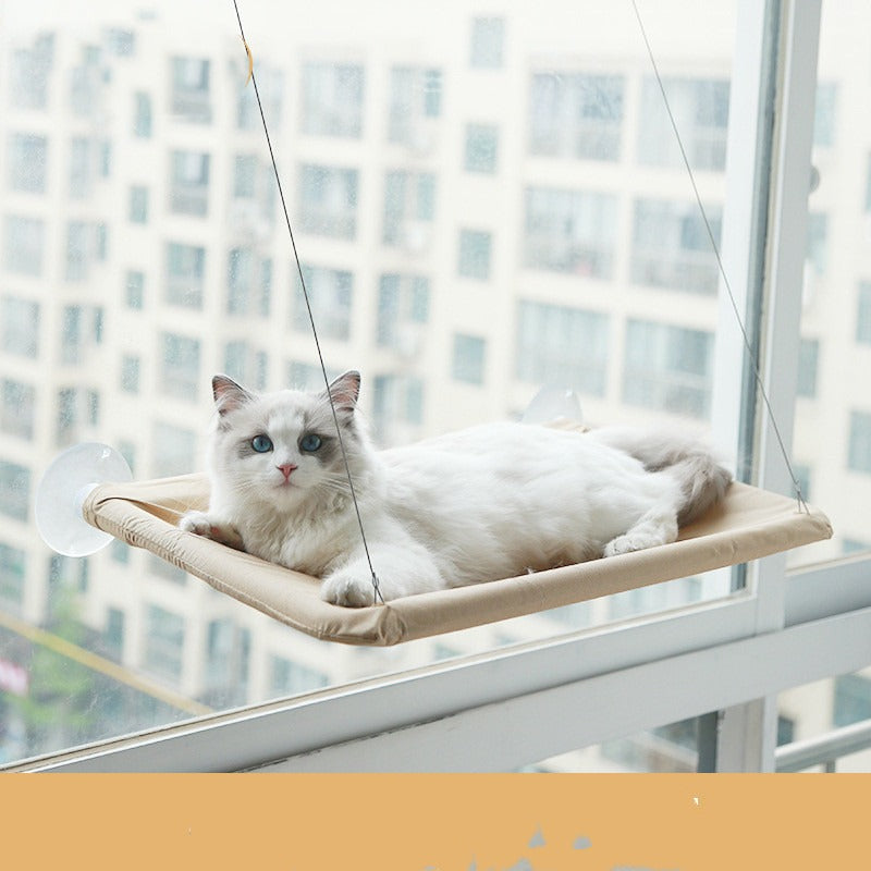 Khaki suction cup cat window hammock mounted on apartment glass with a white cat resting on it