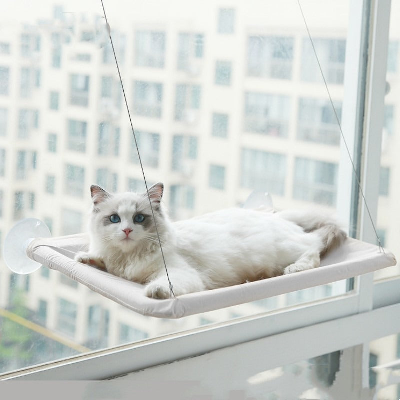 Silver grey suction cup cat window hammock mounted on apartment glass with a white cat resting on it